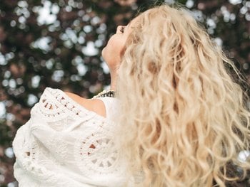 Blonde woman with curly hair against the background of pink cherry blossoms.