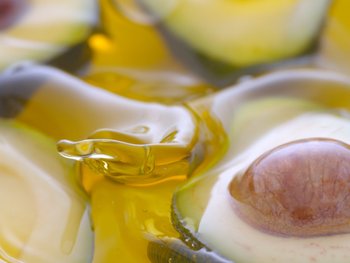 A bottle of pure avocado oil with a blurred avocado in the background, emphasizing its natural origin and beauty benefits.