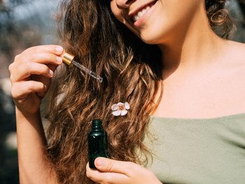 Close-up of brunette model applying hair oil to her long wavy hair.