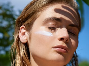 A woman applies sunscreen to her face, indicating the importance of using SPF.