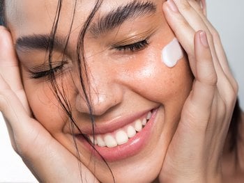 A close-up of a person applying a white moisturizer to their face.