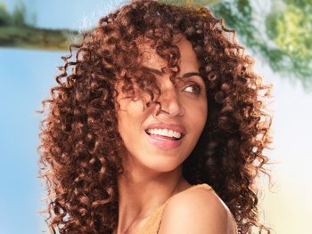 A woman with medium-length, textured brown hair partially obscuring her face.