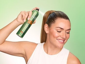 Woman applying hairspray for flexible hold and natural movement.