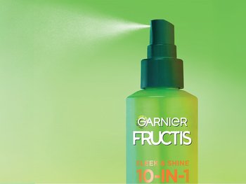 A bottle of Garnier 10-in-1 leave-in spray misting in the air. This product provides reduced flyaways, boosted shine, visible damage reduction and nourishment in one-non greasy formula.