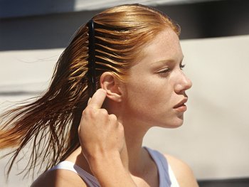 Woman gently combing through her damp, dyed hair.