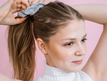 A woman with blonde hair ties her short hair back into a low, slightly messy ponytail.