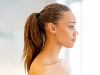A side view of a woman with dark hair pulled back into a sleek, high ponytail.